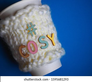 Hand Knit Coffee Cosy With The Word Cosy On Top In Multi Colored Wooden Letters