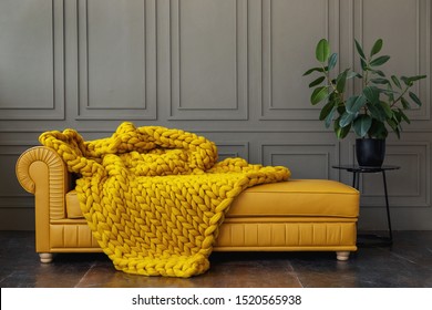 Hand knitted merino wool chunky blanket in interior on background. Stylish and cozy Scandinavian interior: bed, chair, white wall.