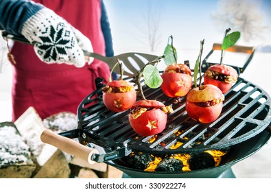 Hand in a knitted mitten cooking stuffed apples with nuts and raisins outdoors over the hot coals of a winter barbecue with a spatula