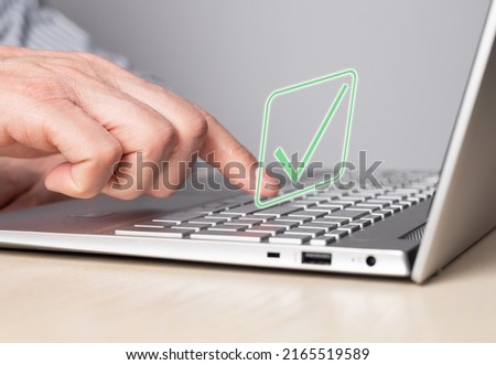 Hand at laptop keyboard with tick icon. Approval of smth, idea, project or online verification of product, service, system or data confirmation. Man forefinger pressing enter button. photo