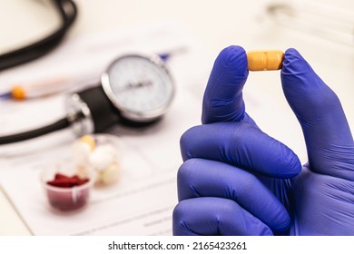 Hand With Latex Glove Holding Tablet Or Pill For Hypertension Treatment, Sphygmomanometer In The Background And Medical Exams