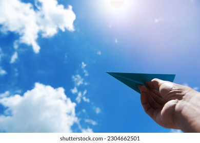 Hand launching paper plane toward cloudy blue sky - Shutterstock ID 2304662501