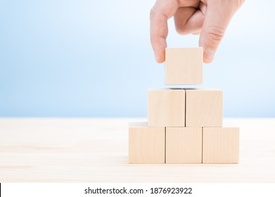 hand lays out builds a pyramid of blank wooden cubes. A cube shape wooden block stacked in pyramid shape without graphics for Business design concept. copy space