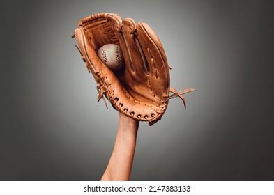 Hand in leather baseball glove caught a ball on dark gray background