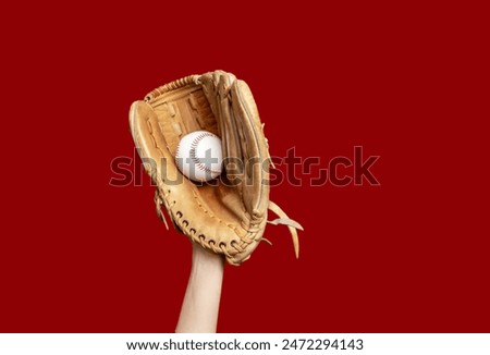 Hand in leather baseball glove holds white baseball on red background. High-quality photo. Winner