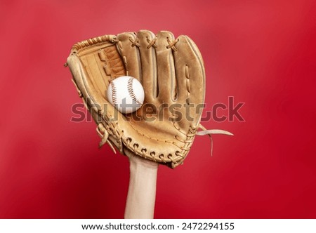Hand in leather baseball glove holds white baseball on red background. High-quality photo. Winner