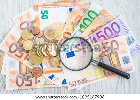 Hand lens on euro banknotes and coins