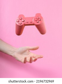 Hand And Levitating Pink Gamepad On Pink Background. Minimalistic Still Life. Concept Art. Video Game