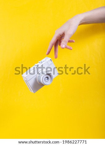 Hand and Levitating white film camera on yellow background. Minimalistic still life. Concept art