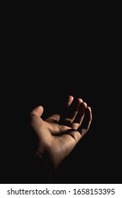 Hand with light and shadows reaching out against a dark background - Shutterstock ID 1658153395