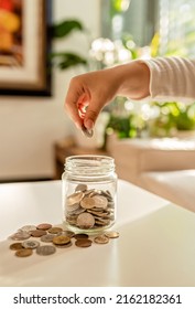 Hand Of Little Child Putting Coin Into Glass Jar. Kid Counting Money Saving From Change Learning Financial Literacy.