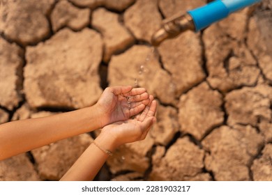 Hand of little girl wating for a drip of water from a faucet at dry ground. Water scarcity and crisis concept. 