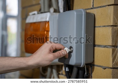 Hand locking outdoor irrigation controller cabinet with a key, side view of automatic watering control box mounted on brick wall.