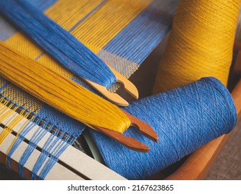 Hand loom with blue and yellow plain weave, two shuttles and yarn, selective focus. Handwoven fabric creation in the process