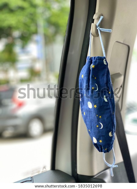 Hand made cotton fabric mask hanging in car by\
the window. Selective focus with background blurred. Concept: New\
normal. Protection from COVID-19. Car provide respite from wearing\
mask while outside.