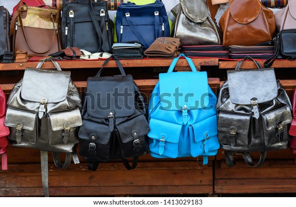 Hand made leather bags and backpacks in\
different colours, black, brown, blue, silver objects, available\
for sale at a traditional weekend\
market\

