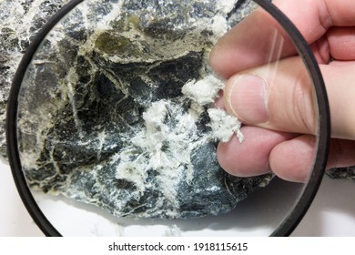 Hand With Magnifying Glass Examines Asbestos Fibers In Stone.