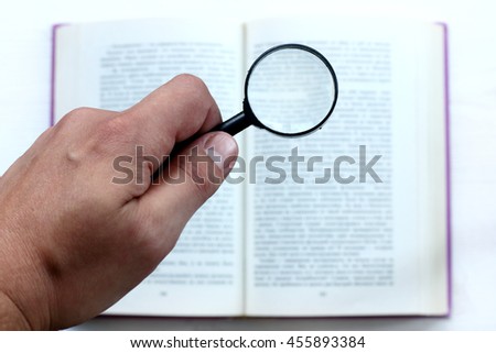 hand with magnifying glass on the background of an open book / thorough examination of information