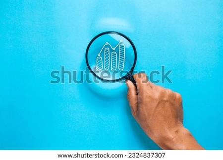 Hand magnifying glass on blue background. graph icon in magnifying glass. financial investment content