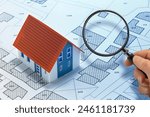 Hand with magnifying glass over cadastral map searching for building lot for building construction, for sale, purchase, rent or investment - Concept with home model and city map.