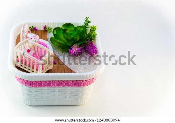 Hand Maid, a hobby pink toy\
room with a cot for baby. The room also has flowers on the white\
sand.