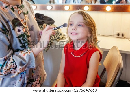Hand of makeup master applying eyeshadow for little pretty girl model. Professional make up applying by artist. Make-up detail in process. Fashon kid beauty salon photosession concept