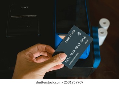 A hand making contactless payment using a black credit card on an EDC card reader machine