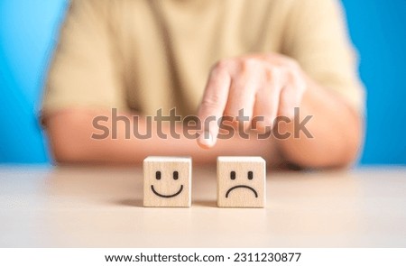 Hand making a decision between two wooden cubes with happy and sad face for positive or negative mindset selection. Emotional state and mental health concept. Like or Dislike for client satisfaction.