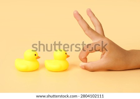 Hand making a flick gesture toward two yellow rubber ducks on a pastel background. Concept of selection, decision making, influence, comparison and human interaction.