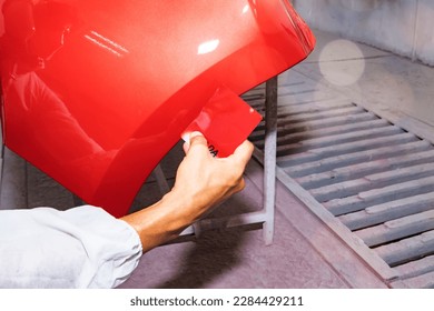 Hand of a male auto painter working car painting room inspects and compares the red paint to the sheet metal sprayed front bumper to get similar and beautiful color : Jobs in auto repair garages. - Powered by Shutterstock