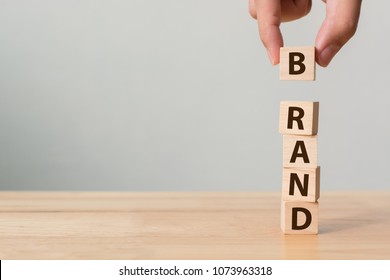 Hand Of Male Putting Wood Cube Block With Word BRAND On Wooden Table. Brand Building For Success Concept