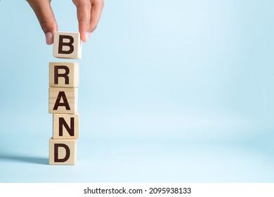 Hand of male putting wood cube block with word BRAND on blue bacground. Brand building for success concept - Shutterstock ID 2095938133