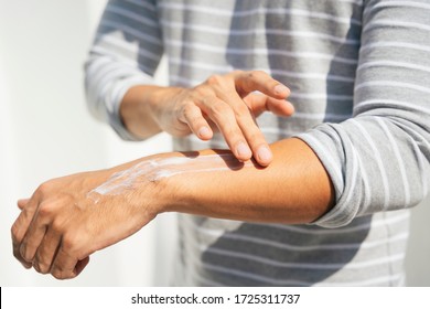 Hand Of A Man Applying Cream Lotion On Arms To Protect The Skin From UV Sunlight. Solar Protection. Sunblock Lotion Bottle. Sun Screen Protection On Man Hand.