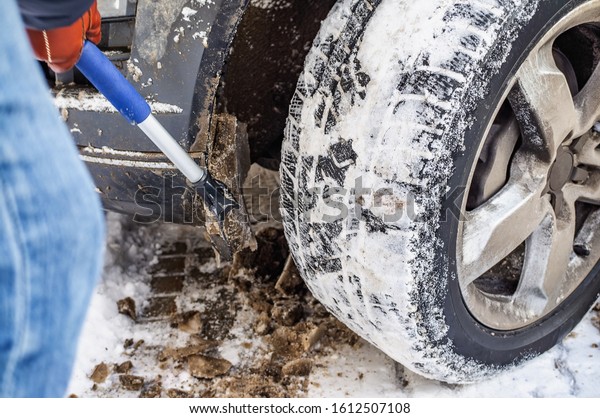 Hand man with a\
brush to clean the car wheels from ice and snow. Car maintenance in\
the period of snow drifts