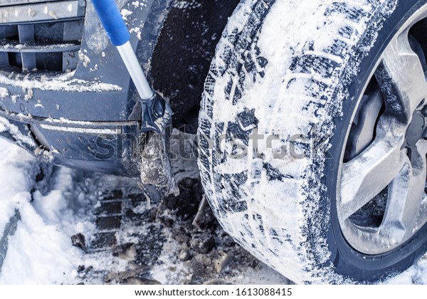 Hand man with a\
brush to clean the car wheels from ice and snow. Car maintenance in\
the period of snow drifts