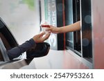 Hand Man in car receiving coffee in drive thru fast food restaurant. Staff serving takeaway order for driver in delivery window. Drive through and takeaway for buy fast food for protect covid19.