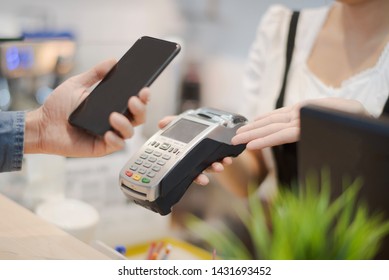 Hand Of Man Customer Using Wireless Or Contactless Payment Of A Smart Phone. Young Asian Cashier Or Seller Are Smiling To Accept Payment By Nfc Technology At Retail Shop. Contactless Payment Concept.