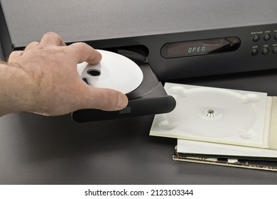 Hand of a man with a disc, an open tray of a CD player. Studio shot, close-up.