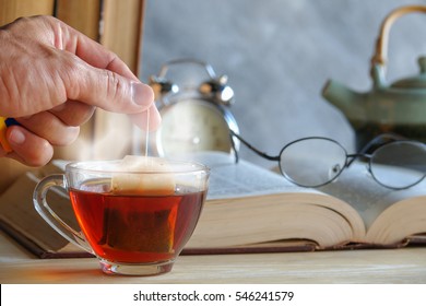 Hand Of Man Dripping Tea Bag In A Tea Cup On Table With Books