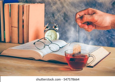 Hand Of Man Dripping Tea Bag In A Tea Cup On Table With Books