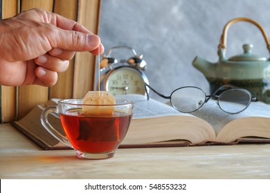 Hand Of Man Dripping Tea Bag In A Tea Cup On Table With Books