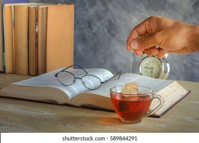 Hand Of Man Dripping Tea Bag In A Tea Cup On Table With Books