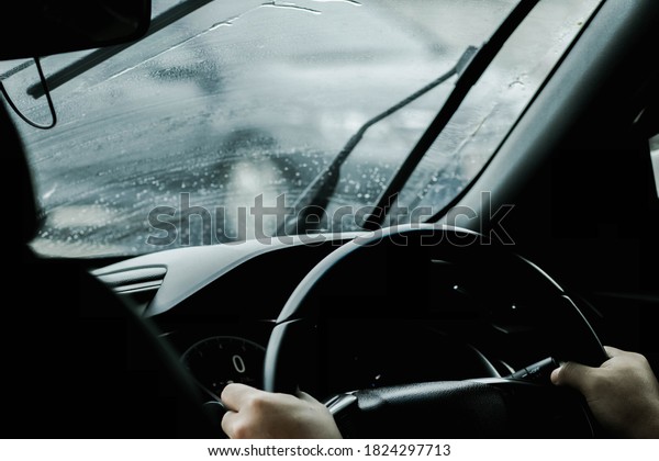 The hand of a man driving on the road on a rainy\
day. hands of a man with car steering wheel is ready on the move in\
the modern life style.
