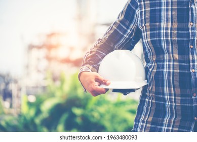 Hand Of Man Engineer Holding Safety Hat (helmet). Safety Officer Inspector In Front Of Refinery Plant. Construction Engineer And Safety And Health Officer Concept. 