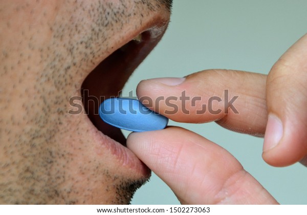 Hand\
of man holding blue pill. Closeup of a man taking blue medicine\
pill. Mouth view, illness. Medicine concept of viagra, medication\
for stomach, erection, sleeping, digestive or\
drugs