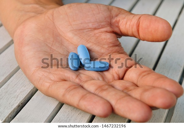 Hand of man holding blue pills. Closeup of a young\
man with a blue pills in one hand. Blue medicine pills. Medicine\
concept of viagra, medication for stomach, erection, sleeping,\
digestive, drugs