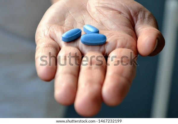 Hand of man holding blue pills. Closeup of a young man\
with a blue pills in one hand. Blue medicine pills. Medicine\
concept of viagra, medication for stomach, erection, sleeping,\
digestive, drugs 