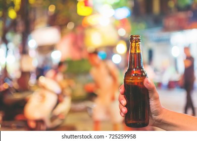 Hand of man holding a brown beer bottle on the night street,copy space.