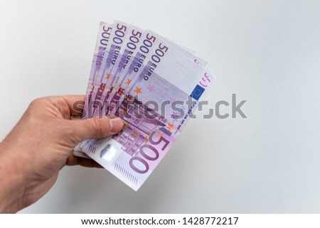 Hand of a man holding a bunch of 500 euro bank notes as reward, credit or side job with a blurred white background