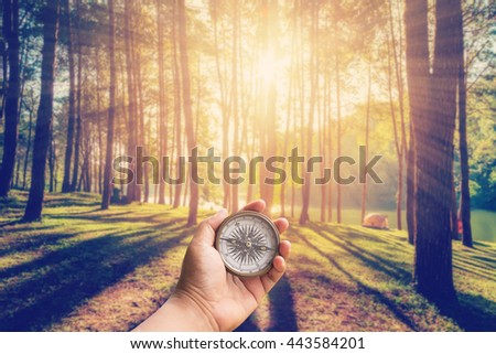 Hand man holding compass at larch forest with sunlight and shadows at sunrise with vintage scene.